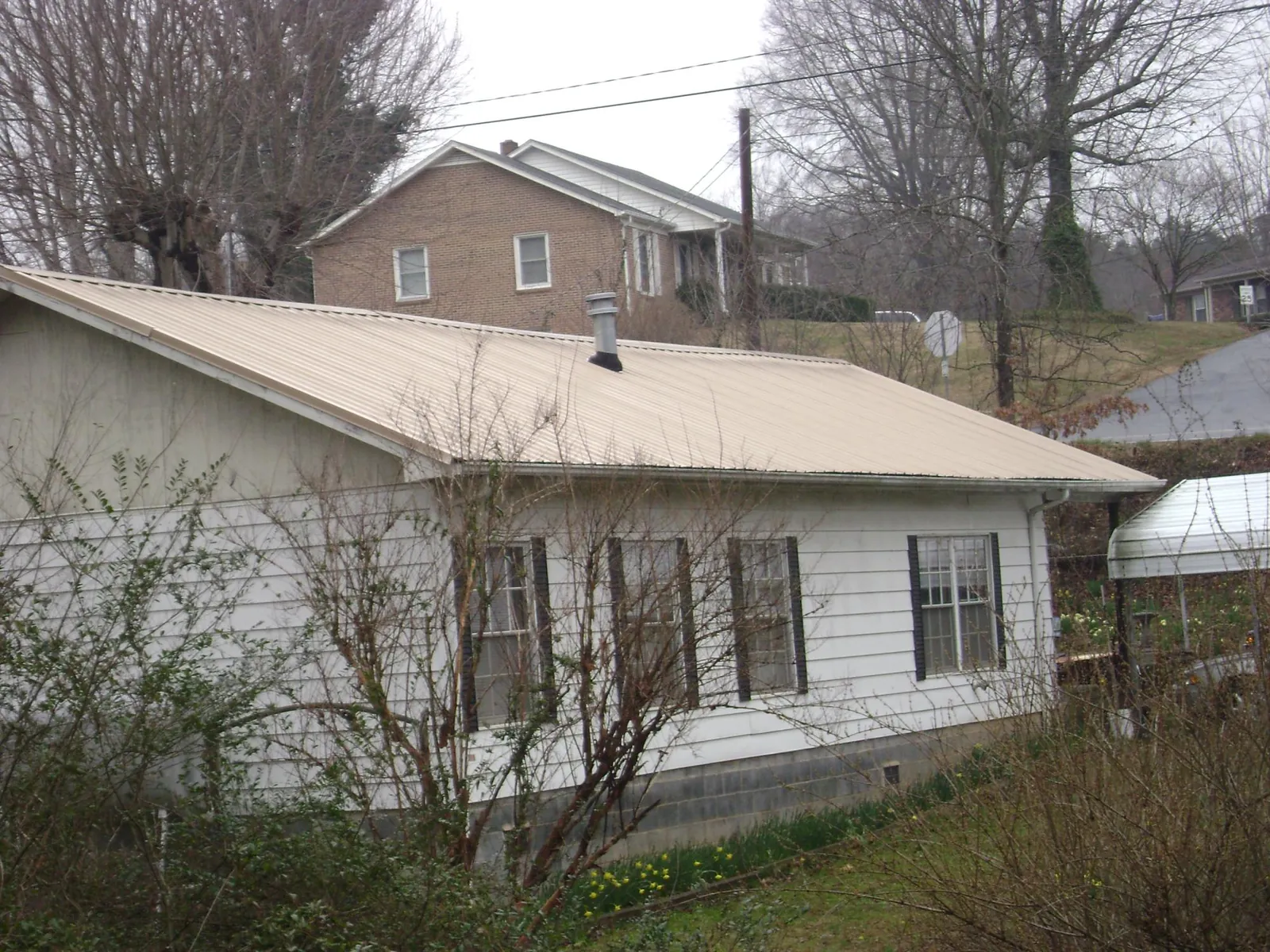 Tan metal roof on a white sided house set into a hillside — Commercial Roofing by Roofing Brothers in National City